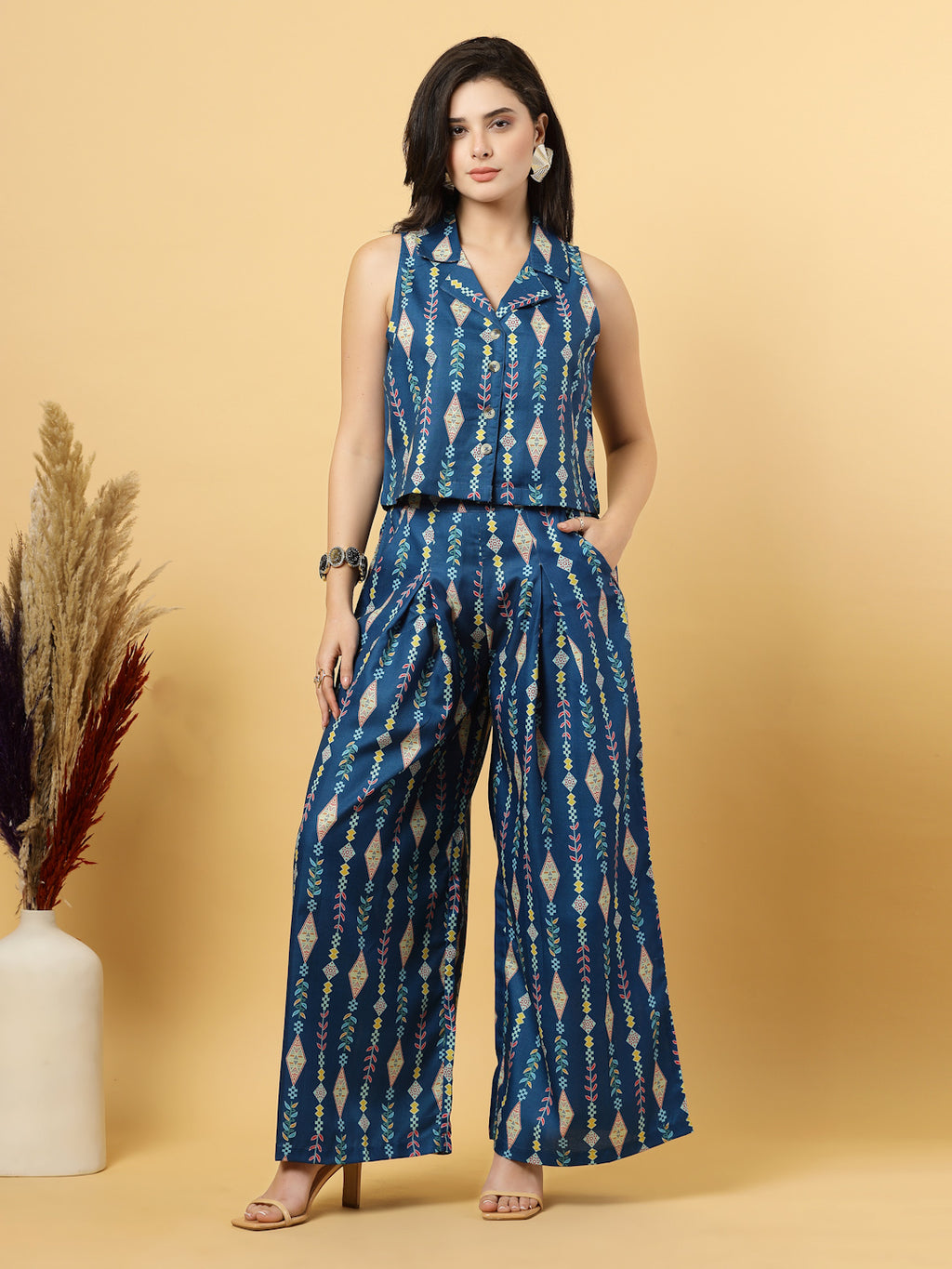 Elevate your ethnic style with this chic 2-piece co-ordinate set for women. The sleeveless top features a beautiful ethnic print with a tailored collar neck and a front button closure for a polished look. Paired with wide-leg pants designed with an elasticated waist, front pleats, and two handy side pockets—this set combines comfort with contemporary flair. Perfect for festive outings or casual gatherings.