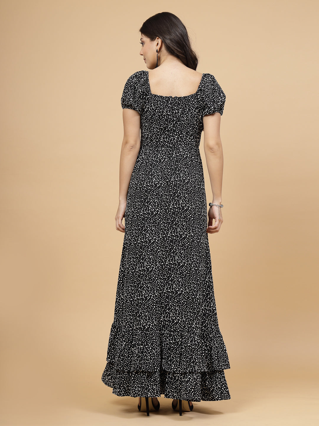 A floor-length casual maxi dress in black dot print. The dress features ruched bust detailing with a drawstring for a customizable fit. It has elasticated shoulders, creating a comfortable and versatile style. The empire waist accentuates the figure, and a double ruffle adds a touch of flair. A front flare with a slit enhances mobility and style. The dress is secured with a zip closure for easy wear.