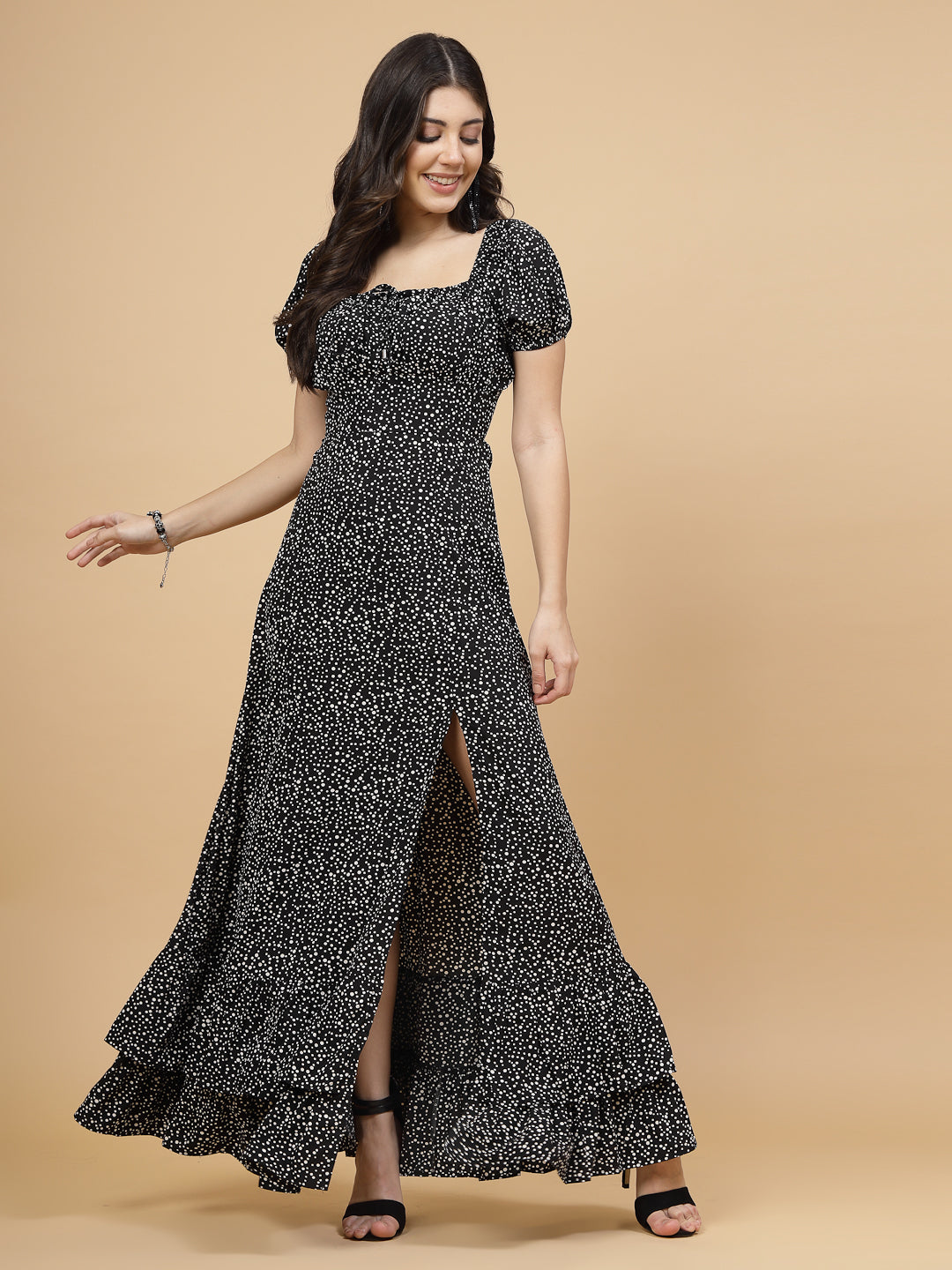 A floor-length casual maxi dress in black dot print. The dress features ruched bust detailing with a drawstring for a customizable fit. It has elasticated shoulders, creating a comfortable and versatile style. The empire waist accentuates the figure, and a double ruffle adds a touch of flair. A front flare with a slit enhances mobility and style. The dress is secured with a zip closure for easy wear.