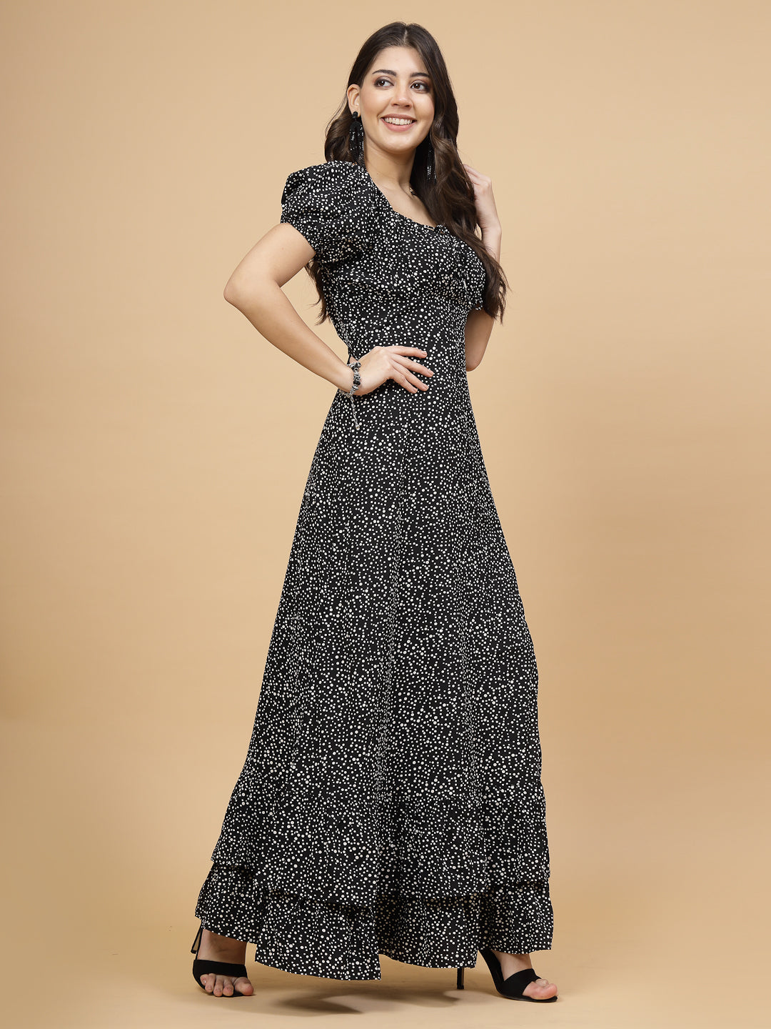 A floor-length casual maxi dress in black dot print. The dress features ruched bust detailing with a drawstring for a customizable fit. It has elasticated shoulders, creating a comfortable and versatile style. The empire waist accentuates the figure, and a double ruffle adds a touch of flair. A front flare with a slit enhances mobility and style. The dress is secured with a zip closure for easy wear.