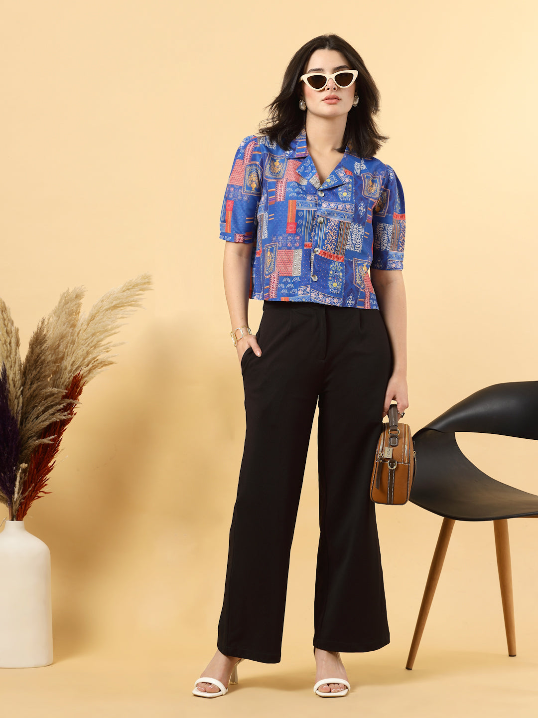 A woman is standing and posing with a blue colour printed coat collar top in a patterned design. 