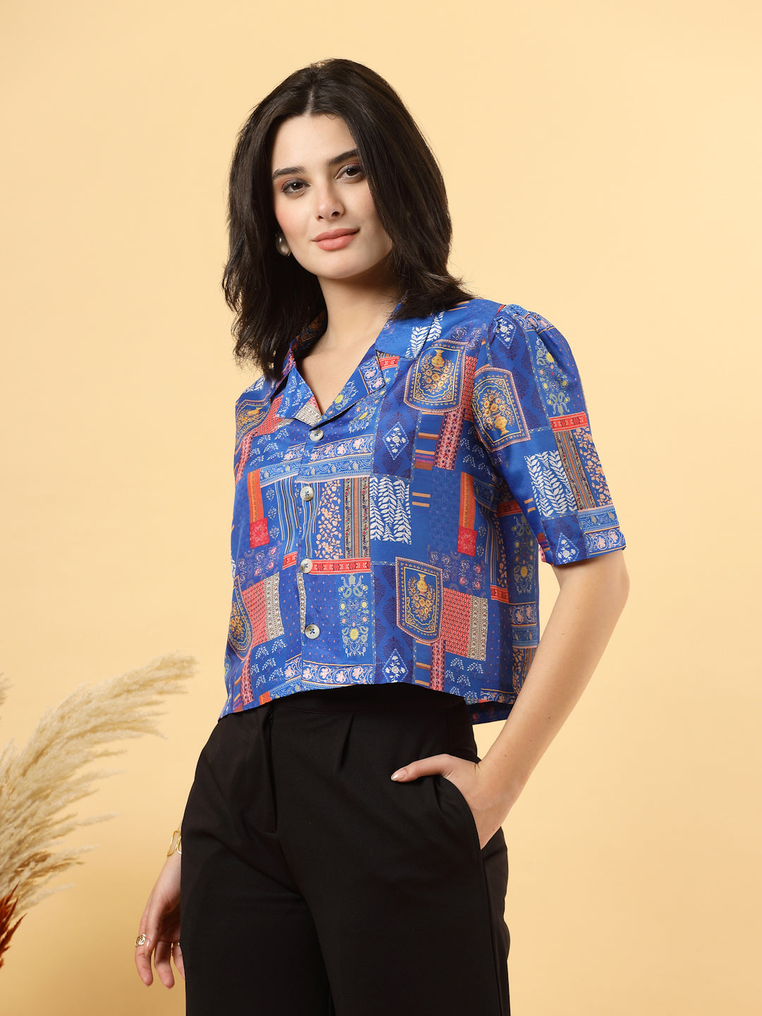 A woman is standing and posing with a blue colour printed coat collar top in a patterned design. 