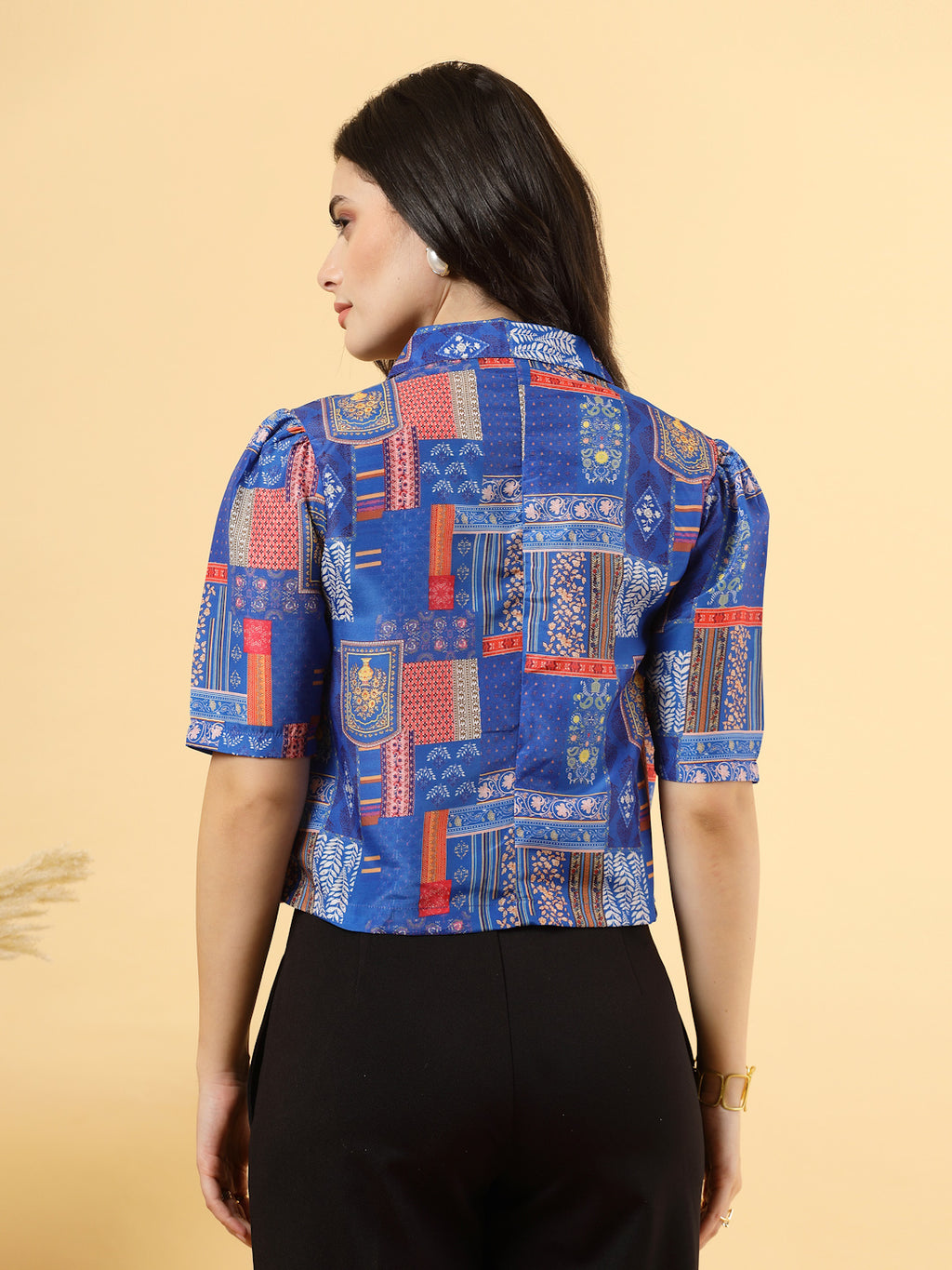 A woman is standing and posing with a blue colour printed coat collar top in a patterned design. 