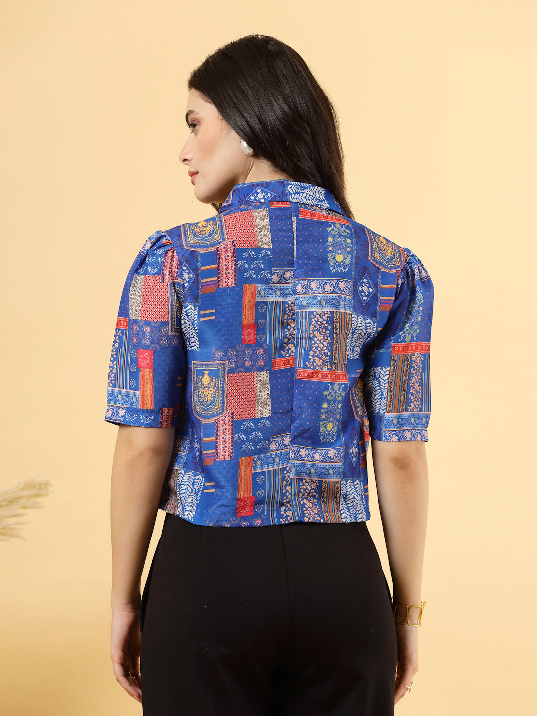 A woman is standing and posing with a blue colour printed coat collar top in a patterned design. 