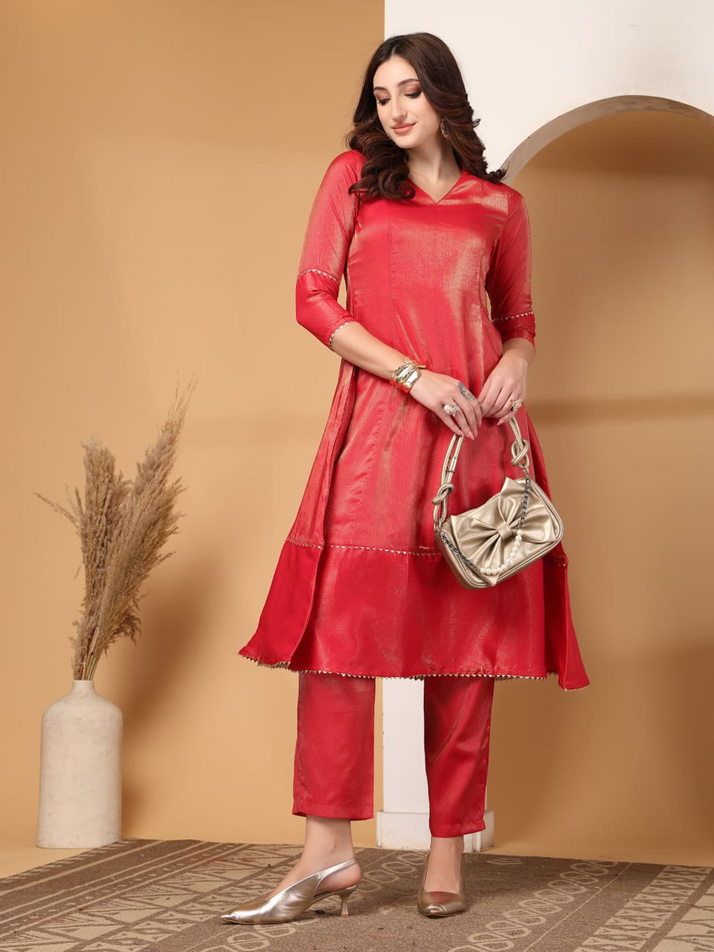 Woman wearing a festive red flared A-line kurti with vertical gold metallic stripes, delicate gota lace trimming, and matching red trousers. Front View