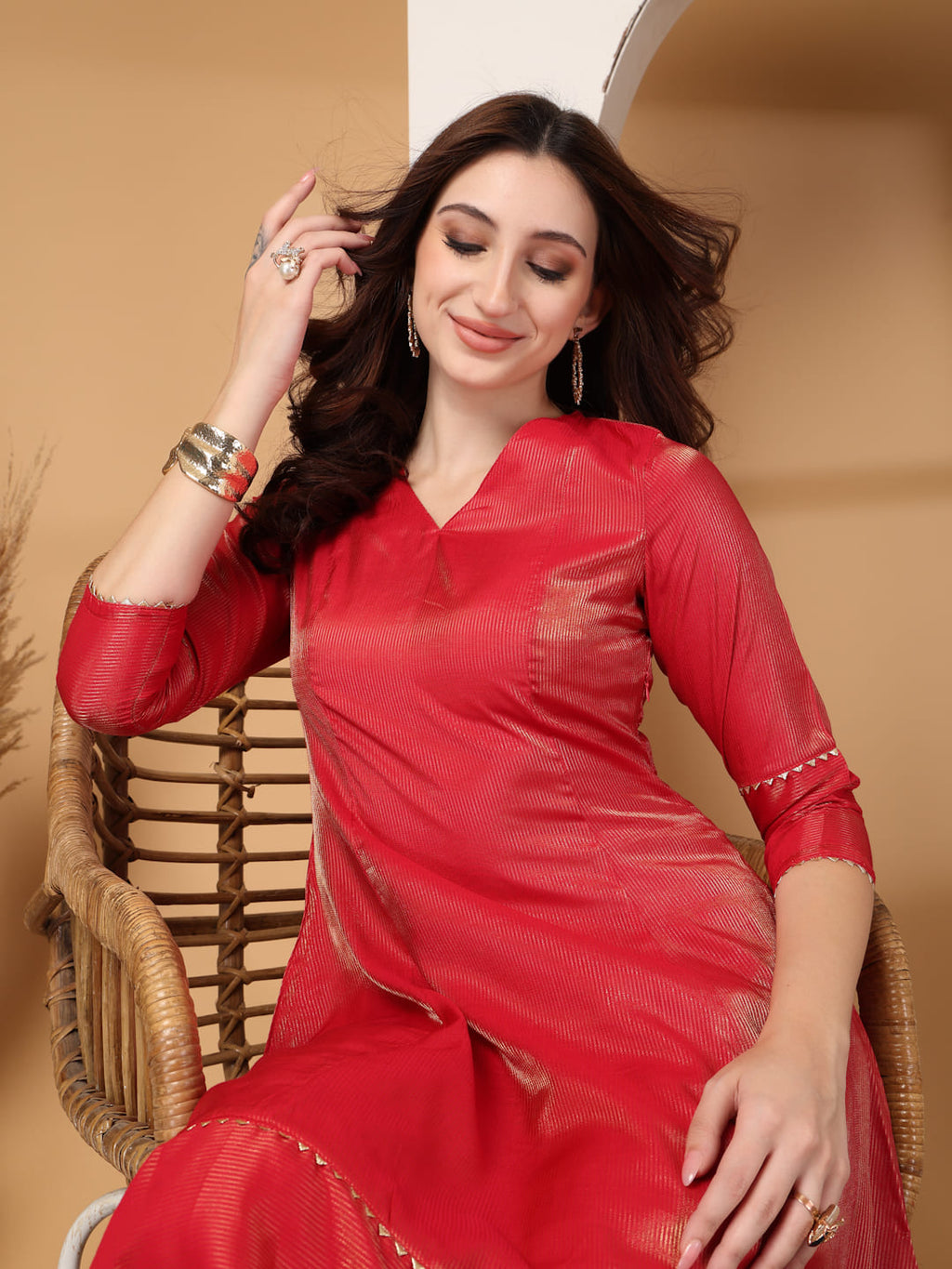 Woman wearing a festive red flared A-line kurti with vertical gold metallic stripes, delicate gota lace trimming, and matching red trousers. Sitting Close up