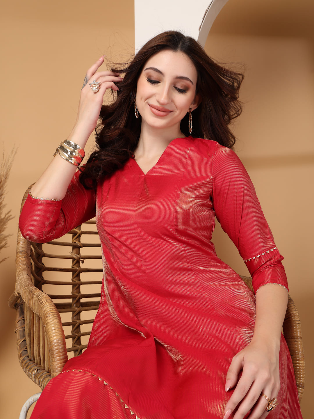 Woman wearing a festive red flared A-line kurti with vertical gold metallic stripes, delicate gota lace trimming, and matching red trousers. Sitting Close up