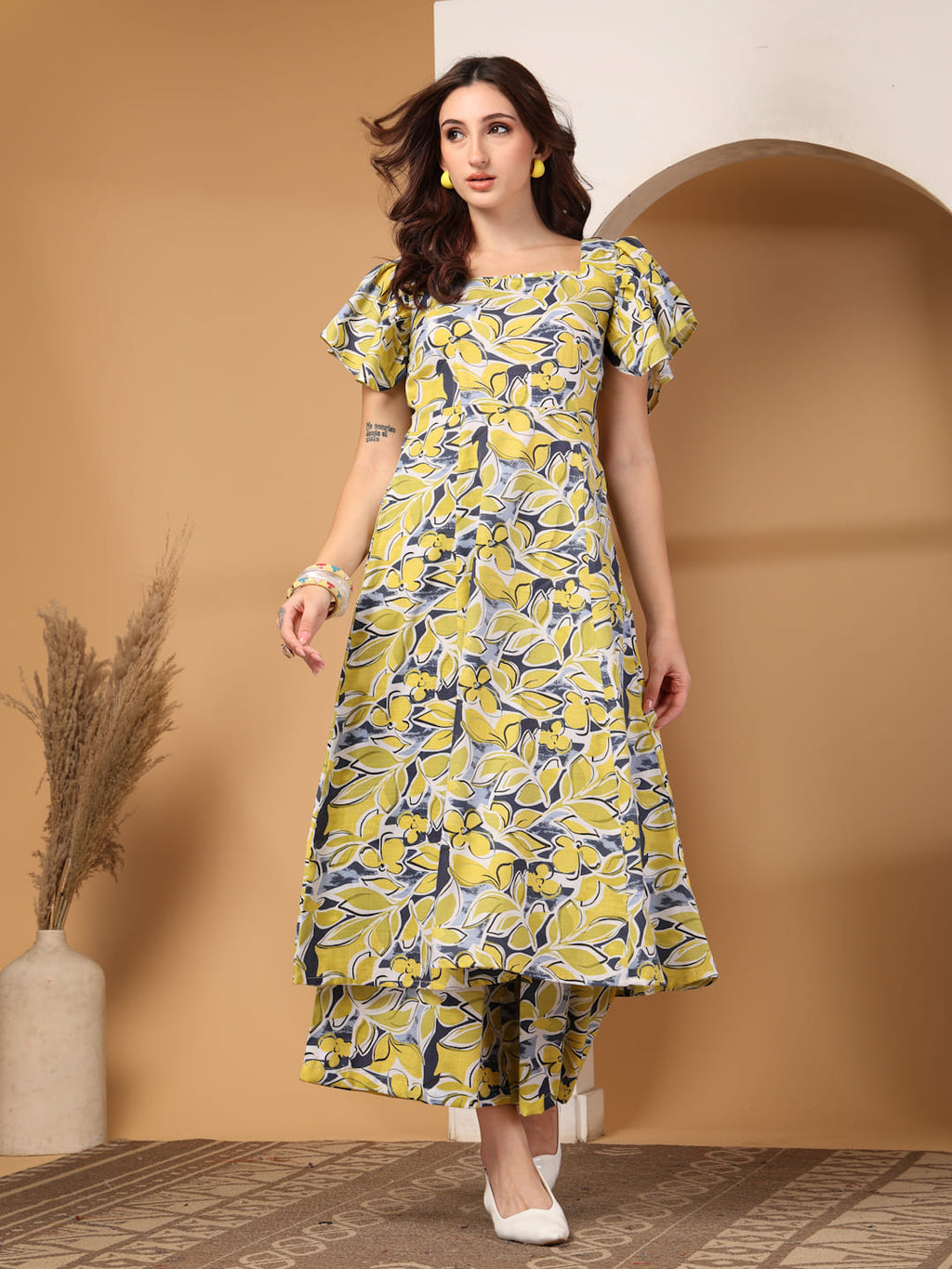 Woman wearing a yellow & grey floral printed square neck kurti with flutter sleeves and matching trousers.