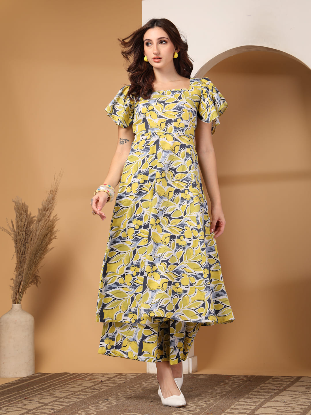 Woman wearing a yellow & grey floral printed square neck kurti with flutter sleeves and matching trousers.