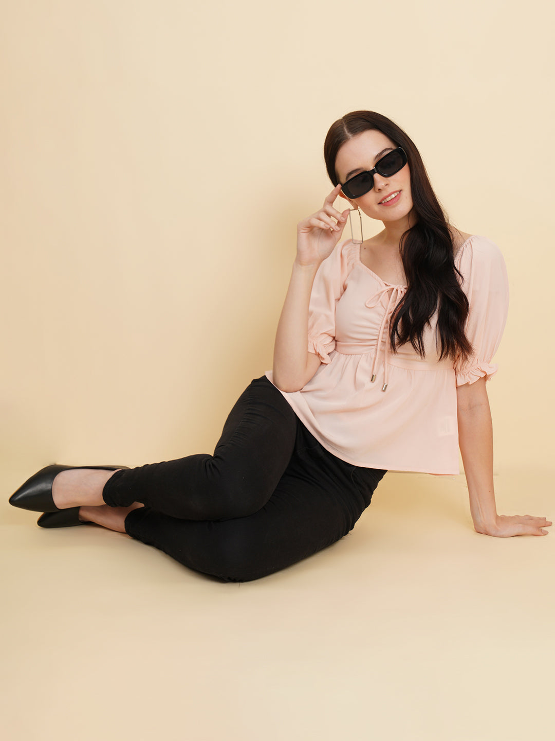 A peach-colored solid peplum top for women with ruched waist detailing. The top features a flattering peplum silhouette that cinches at the waist and flares out, creating a feminine and stylish look. The peach color adds a soft and elegant touch to the garment.