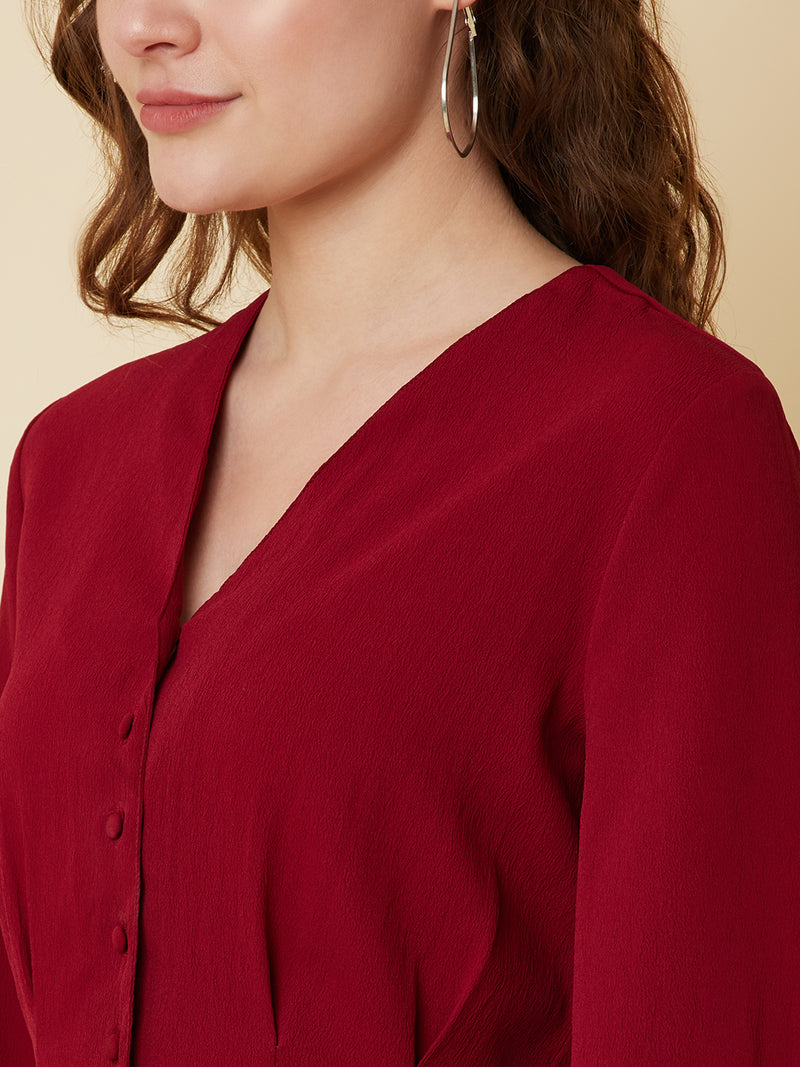 This top is made of a burgundy colored fabric and features a solid waist and pleated detailing. The waist creates a flattering silhouette by accentuating the waistline, while the pleats add texture and dimension to the top. The neckline is V shape and the sleeves are full, making this top perfect for both casual and formal occasions. It can be paired with jeans or dress pants, and can be dressed up or down depending on the occasion.