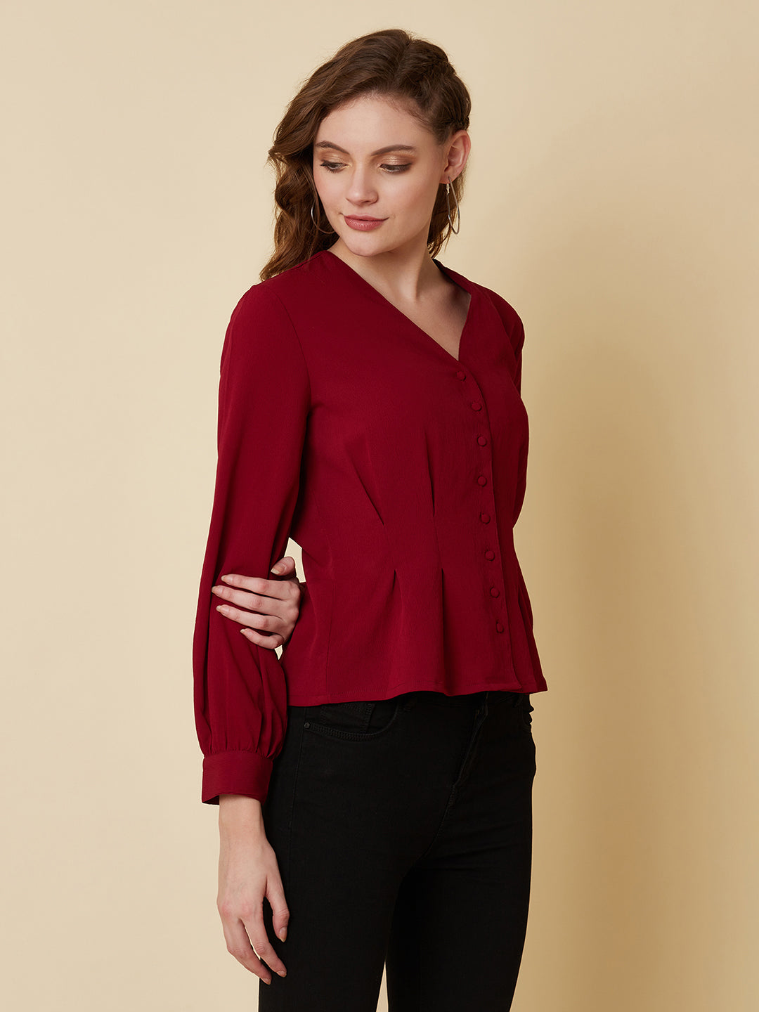 This top is made of a burgundy colored fabric and features a solid waist and pleated detailing. The waist creates a flattering silhouette by accentuating the waistline, while the pleats add texture and dimension to the top. The neckline is V shape and the sleeves are full, making this top perfect for both casual and formal occasions. It can be paired with jeans or dress pants, and can be dressed up or down depending on the occasion.